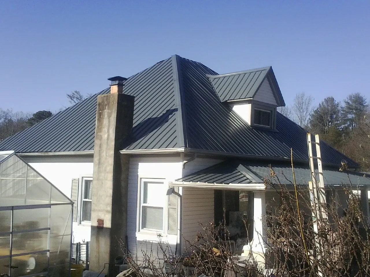 Dark blue standing seam metal roof on a white farmhouse with dormer — Slate & Tile Roof Repair by Roofing Brothers in Chadwick