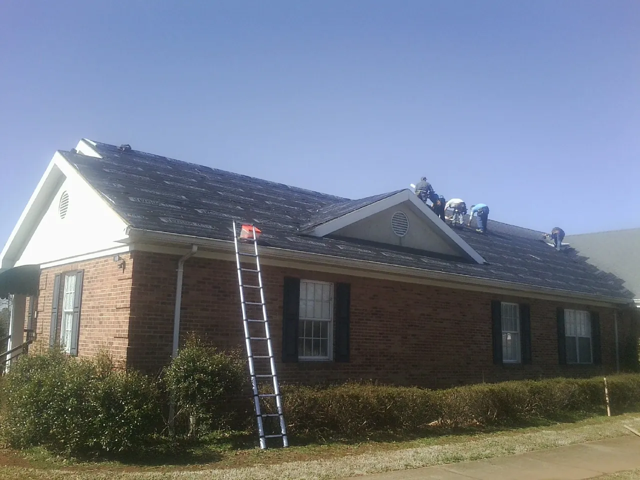 Crew tearing shingles off a brick ranch roof with a ladder set — Metal Roof Repair work by our crew in Chadwick