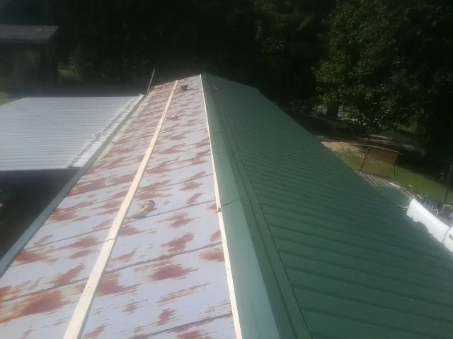 Old rusted panels beside newly installed green metal roofing — Wind Damage Roof Repair by Roofing Brothers in Chadwick