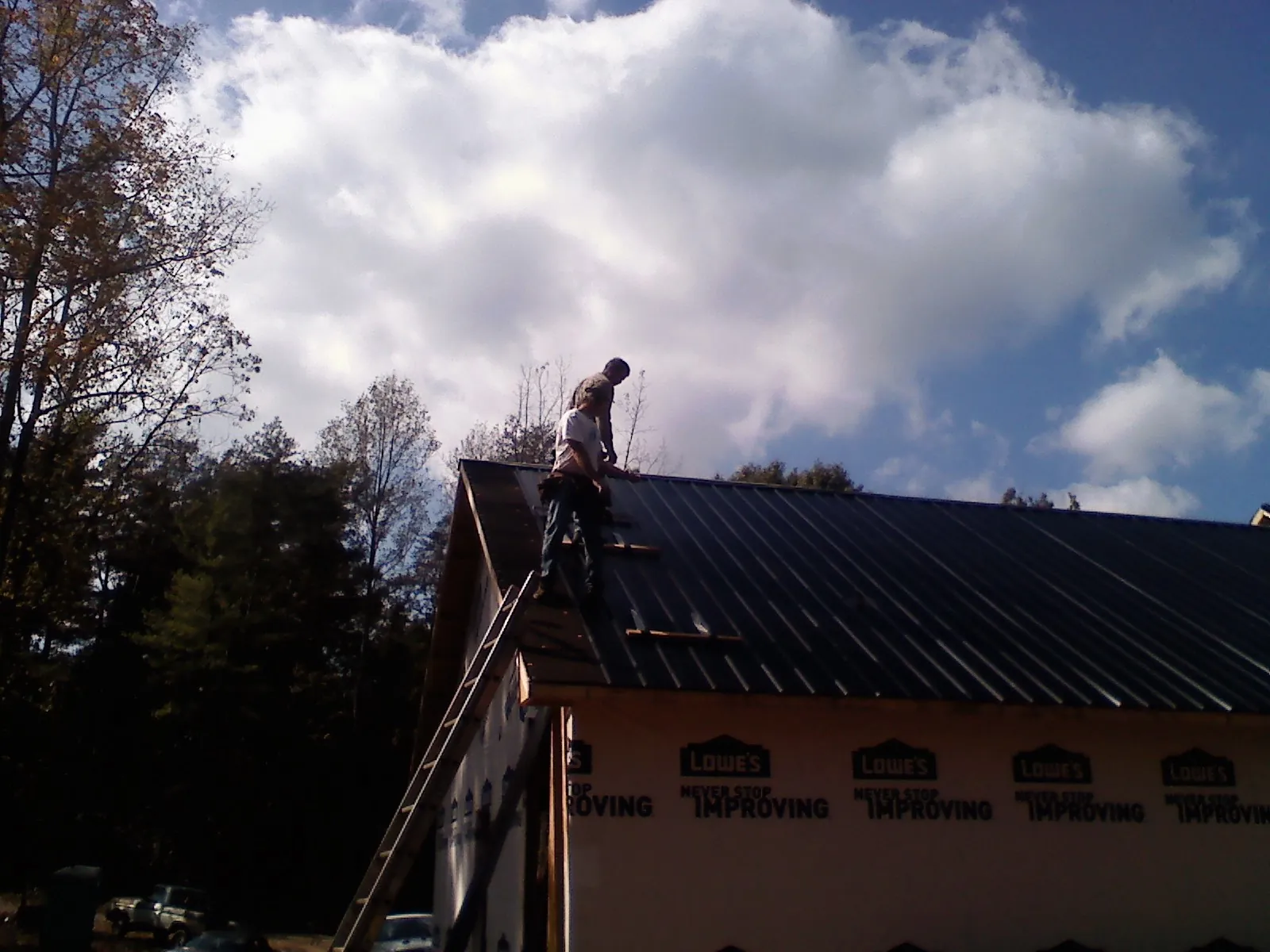 Roofer fastening dark metal panels high against a cloudy sky, from a Roof Inspection job in Chadwick
